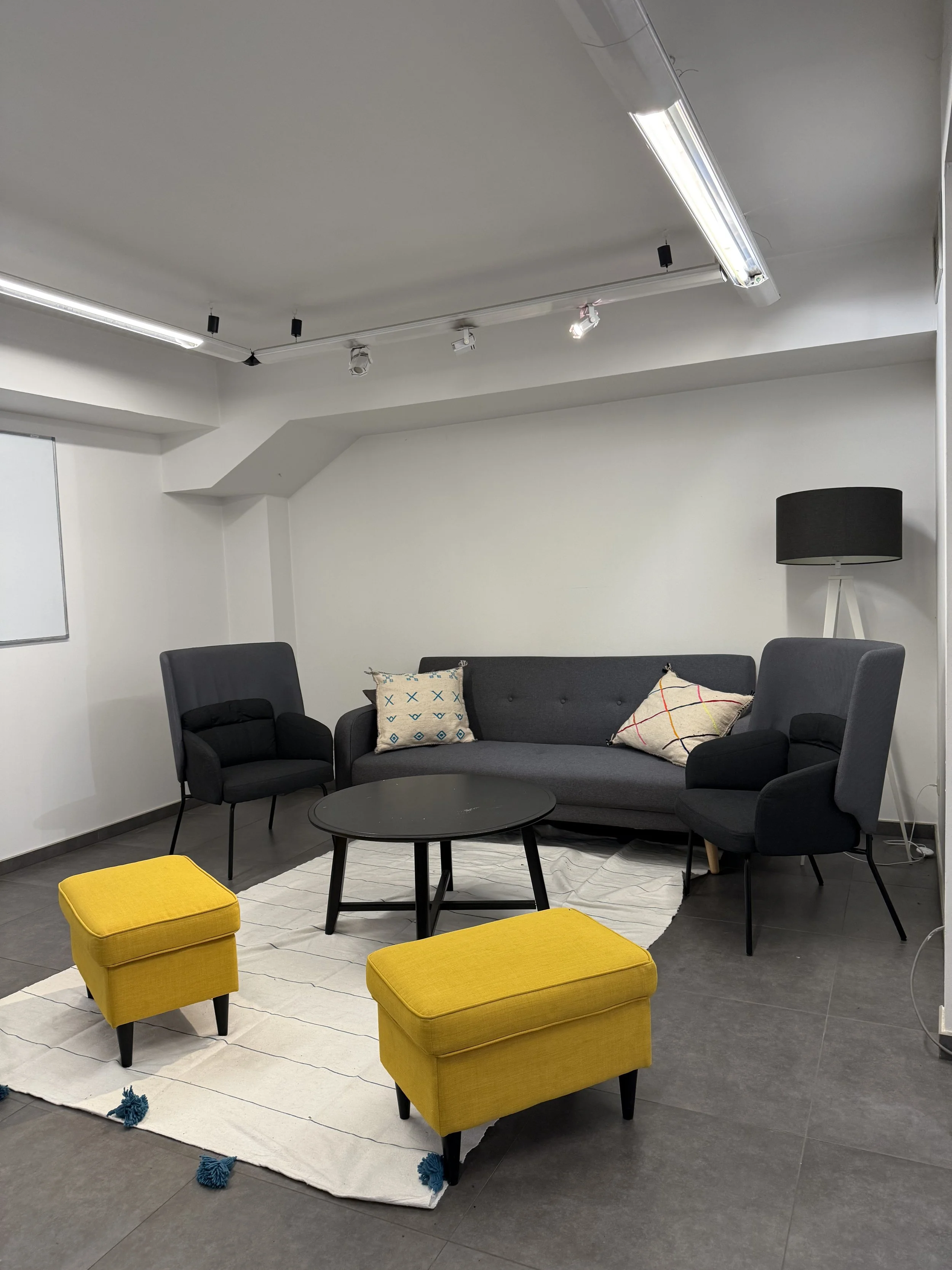 Deux femmes discutent dans une salle de réunion, une assise sur un canapé avec un ordinateur portable, l'autre tenant une tasse, à côté d'une table ronde jaune.
