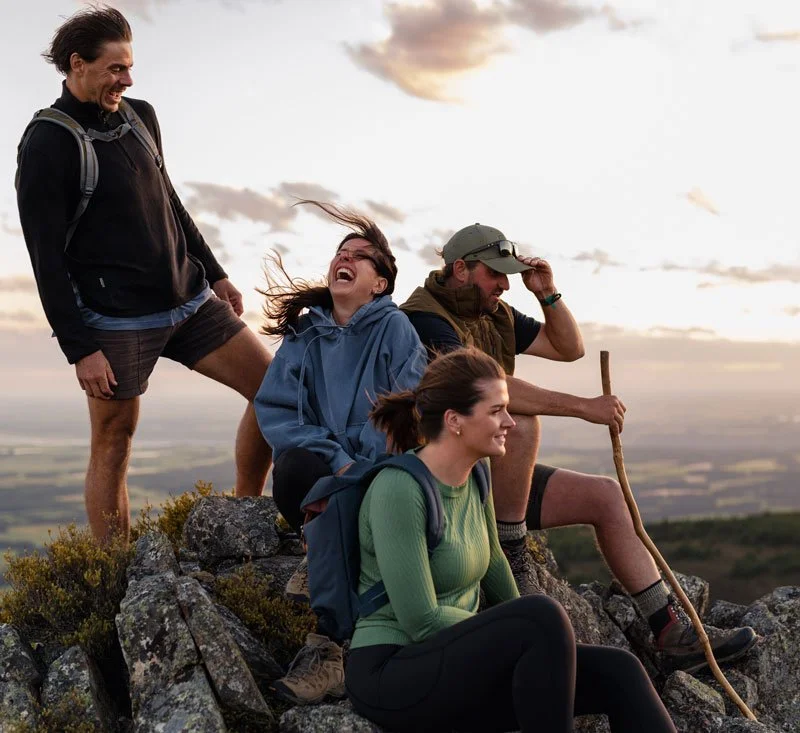 Four friends enjoying a moment on at RockRidge walk during sunset, with one holding a hiking stick and all smiling or laughing.