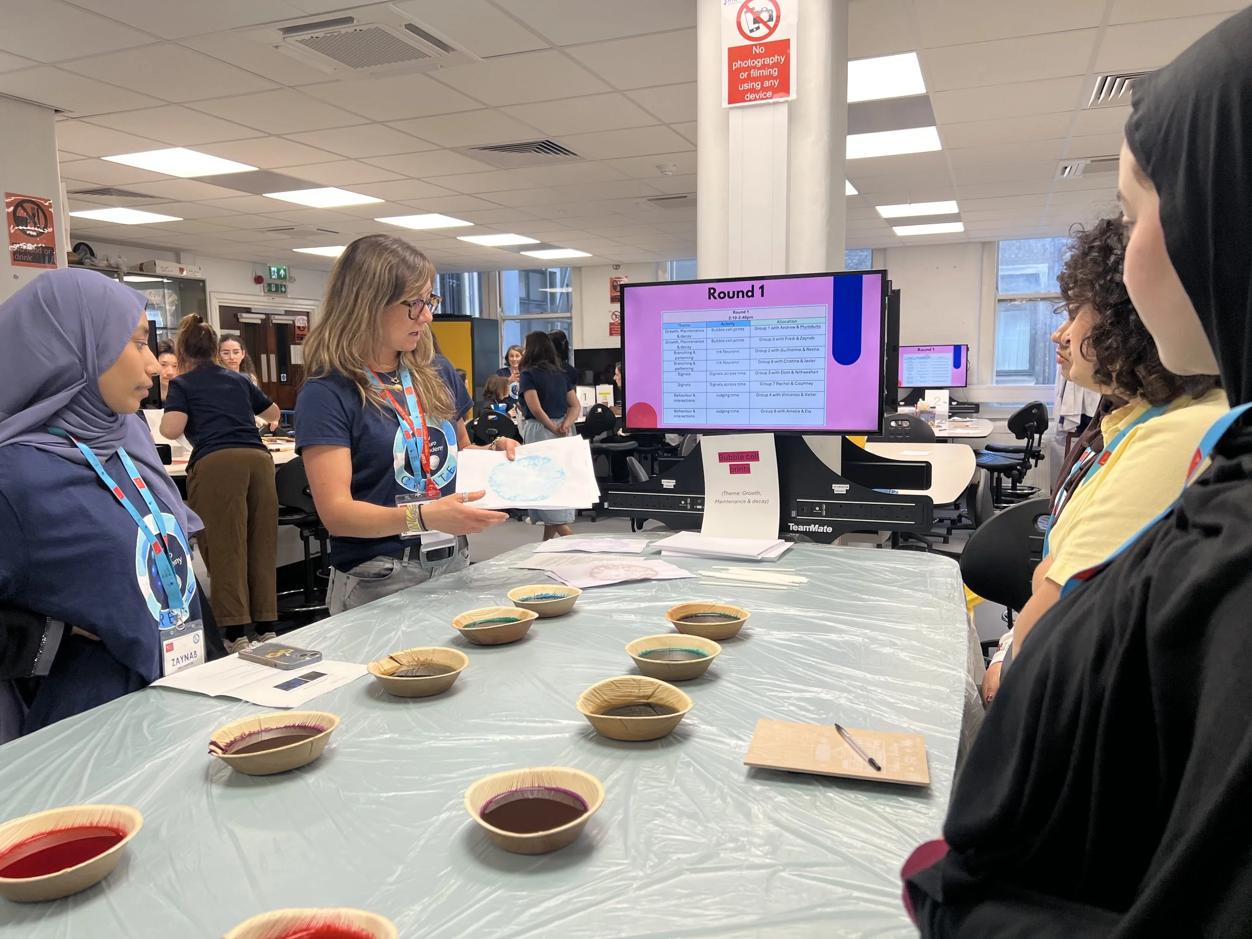 A tutor holds paper over bowls of colourful ink.