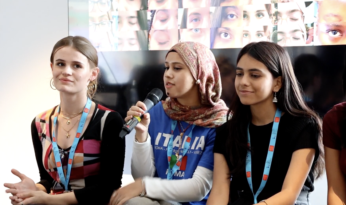 Participants sit in a line with a mic answering questions.