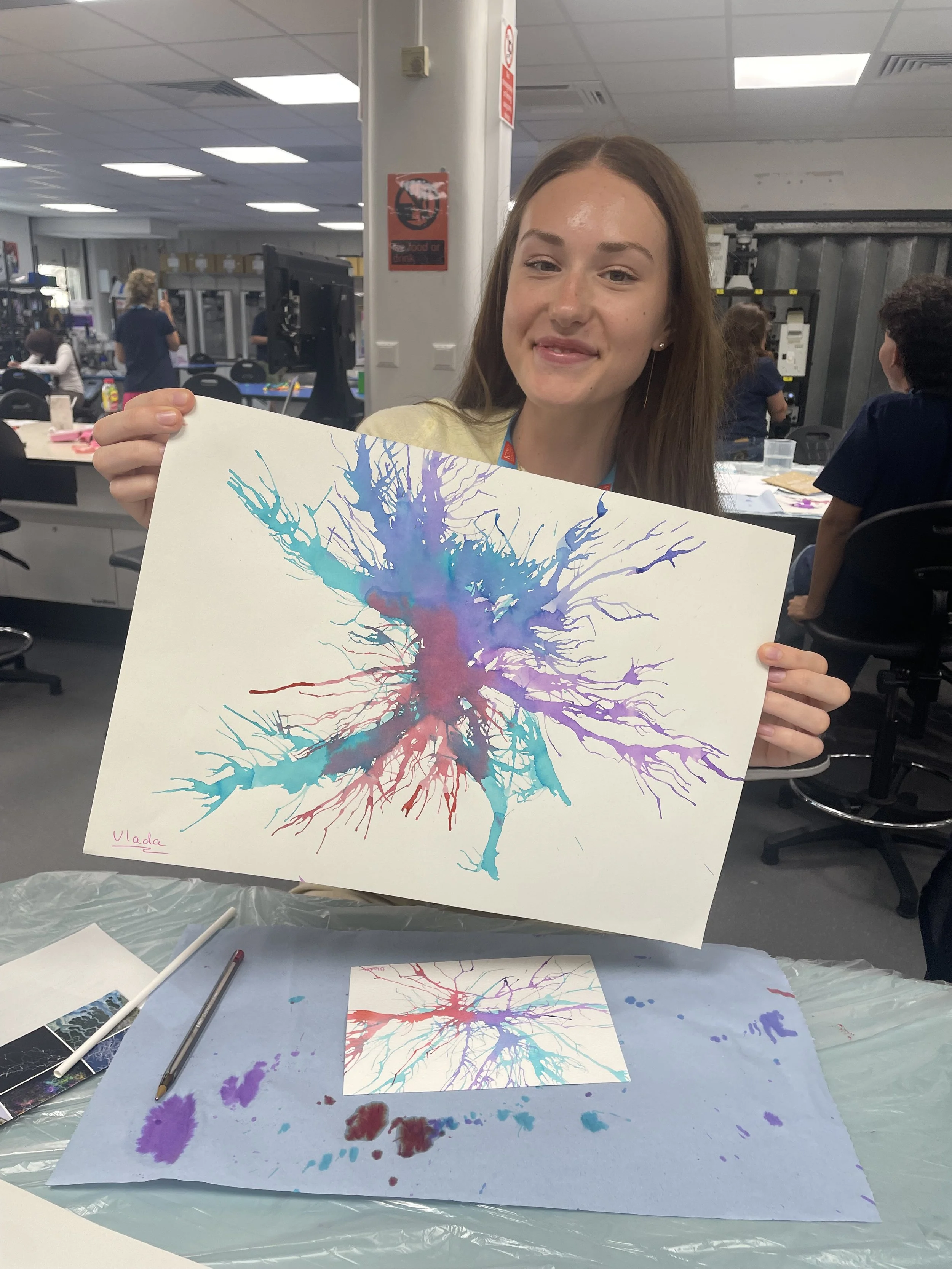 A participant smiles and holds up an ink neuron image.