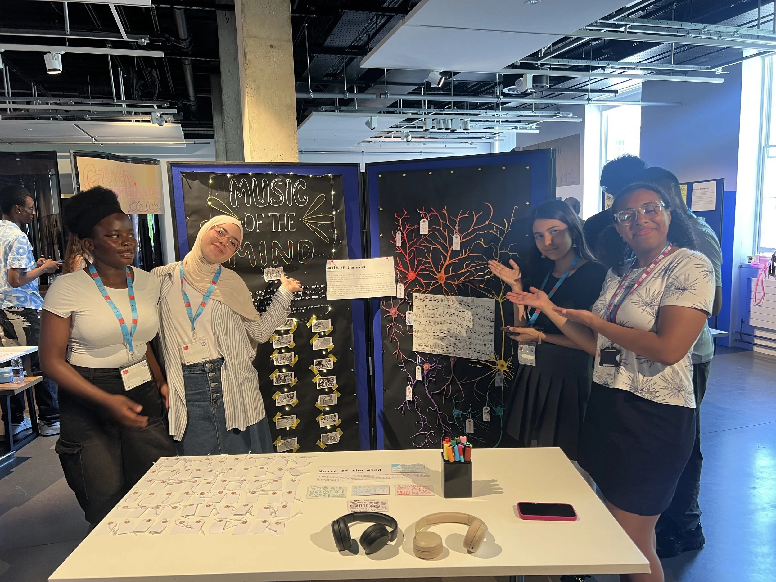 The Music of the Mind group standing around and pointing at their installation. A large black sheet with a colourful neuron tree.