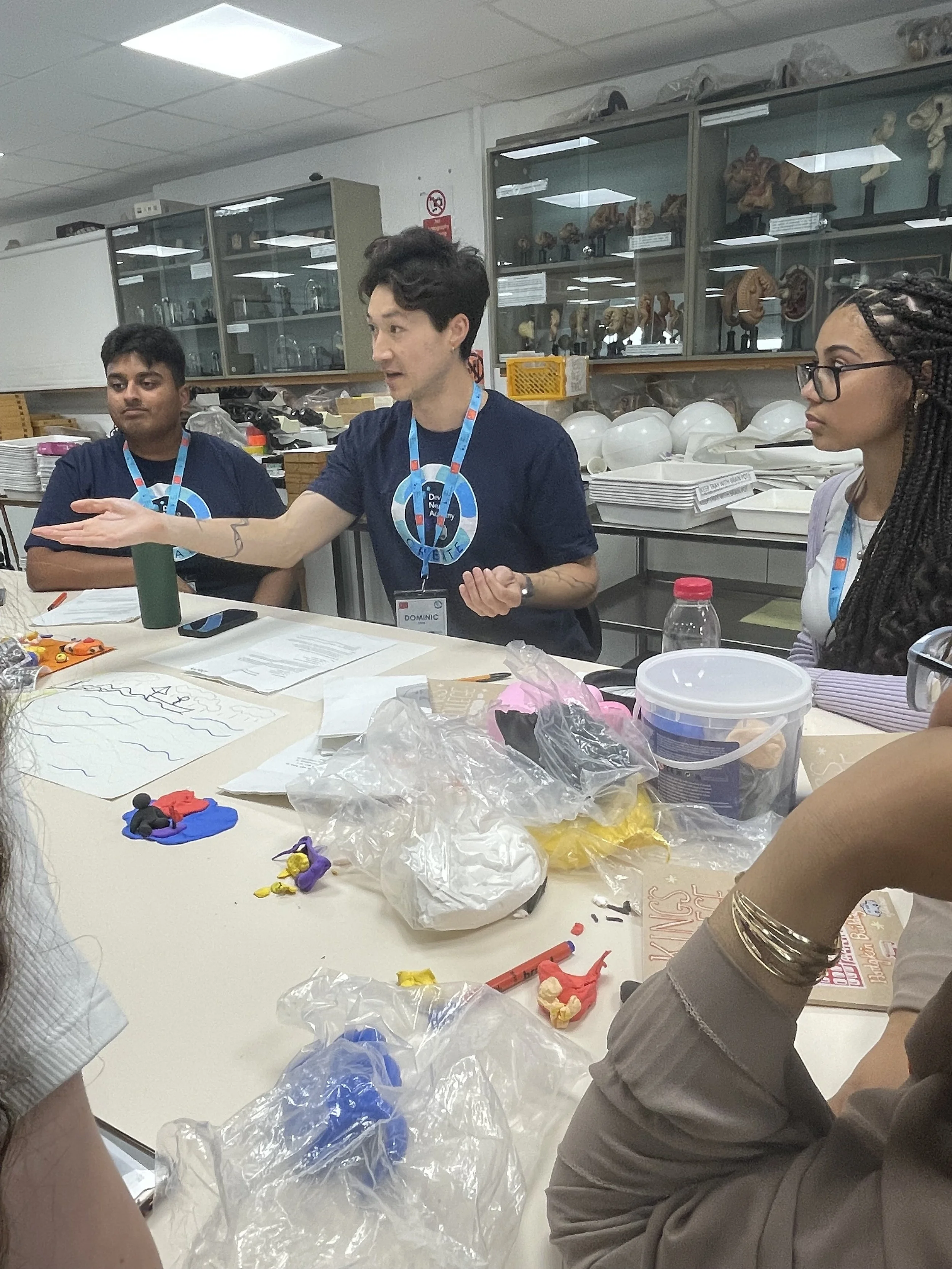 A tutor gestures to pieces of paper and plasticine images.
