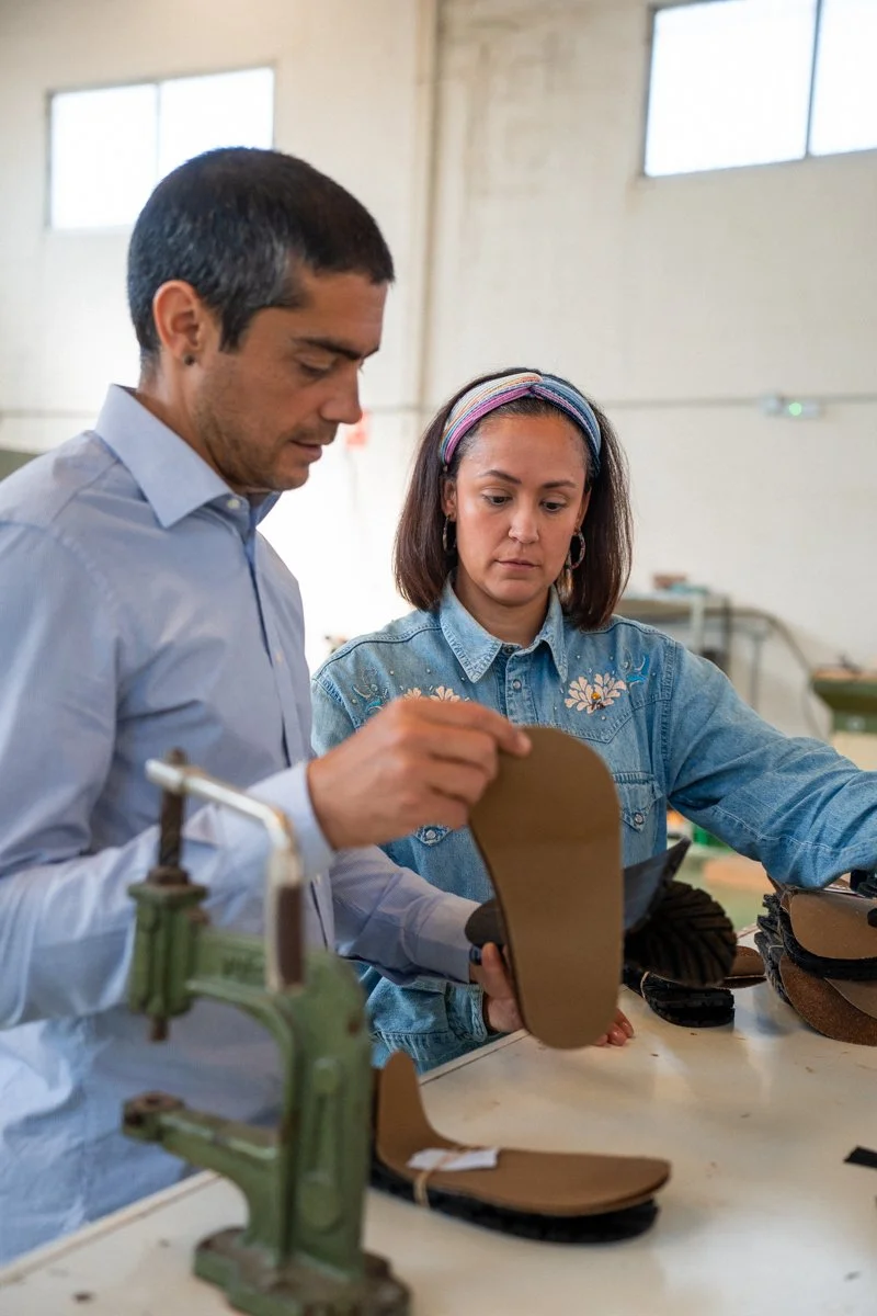 Dos personas en una fábrica evaluando plantillas de zapatos.