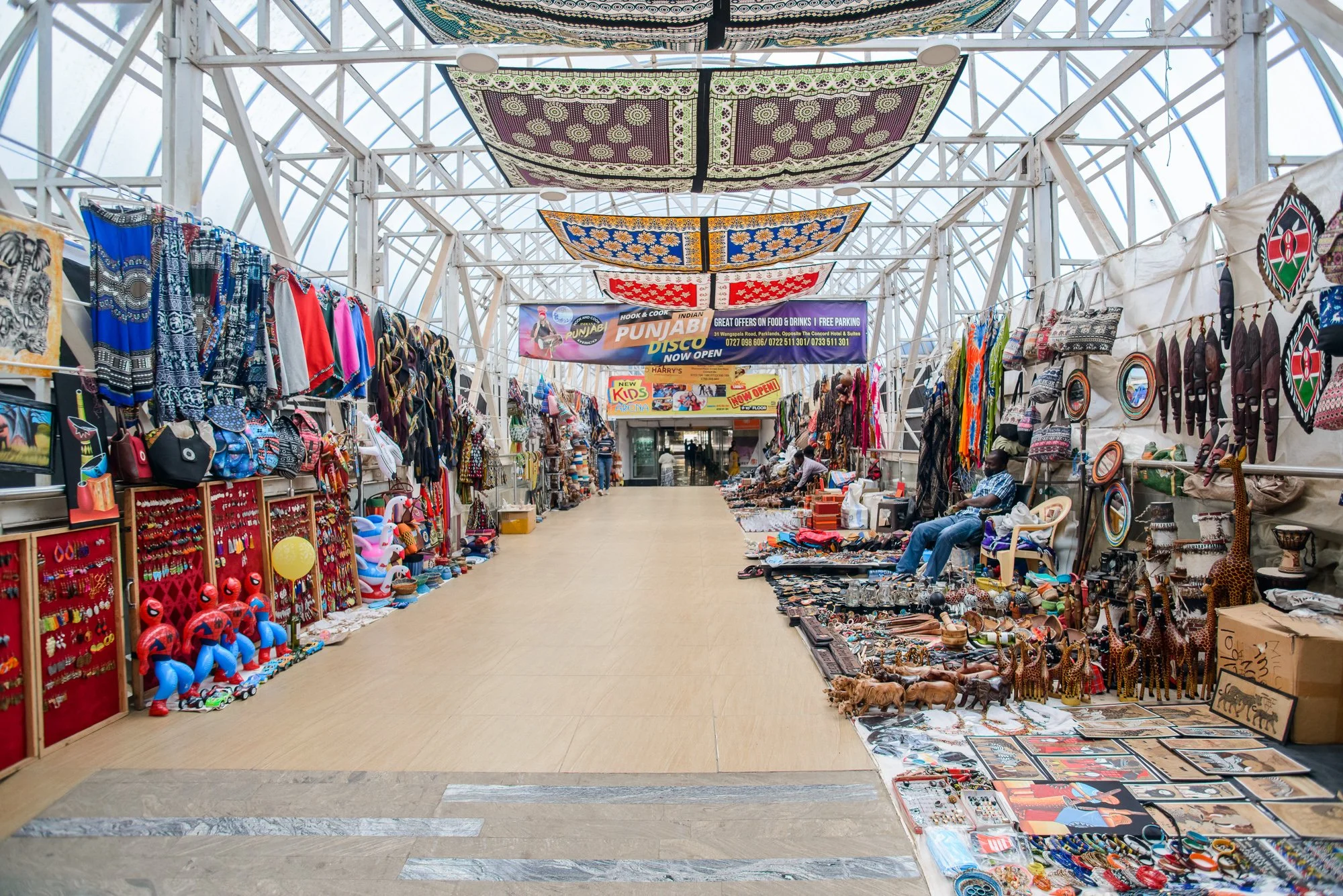 Indoor market with various stalls selling colorful clothing, jewelry, souvenirs, and artisanal crafts.