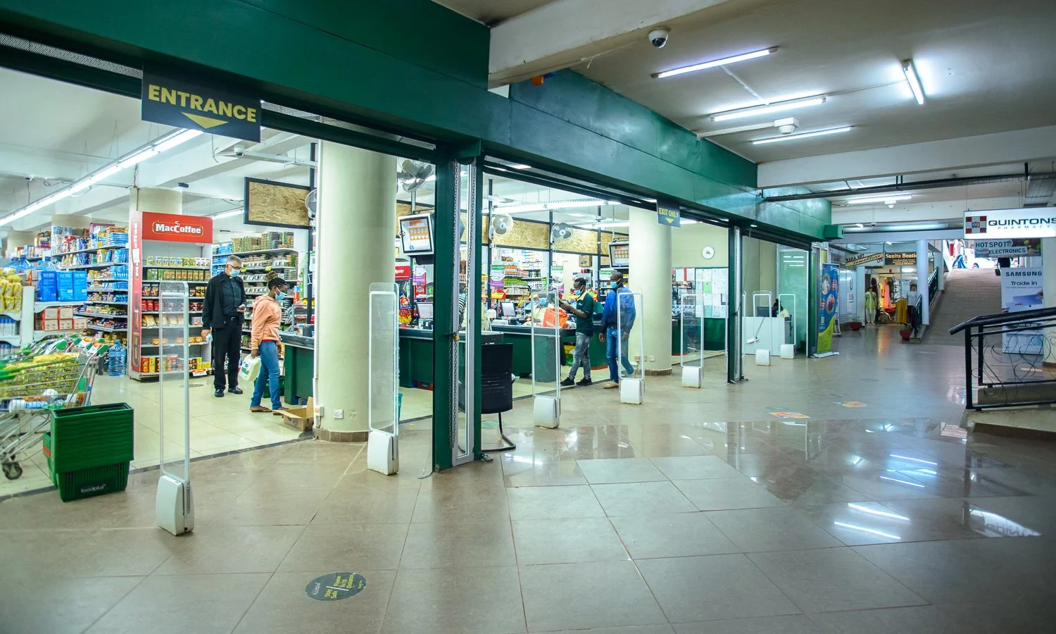 Entrance of a grocery store with people shopping inside and signs indicating the entrance and exit.