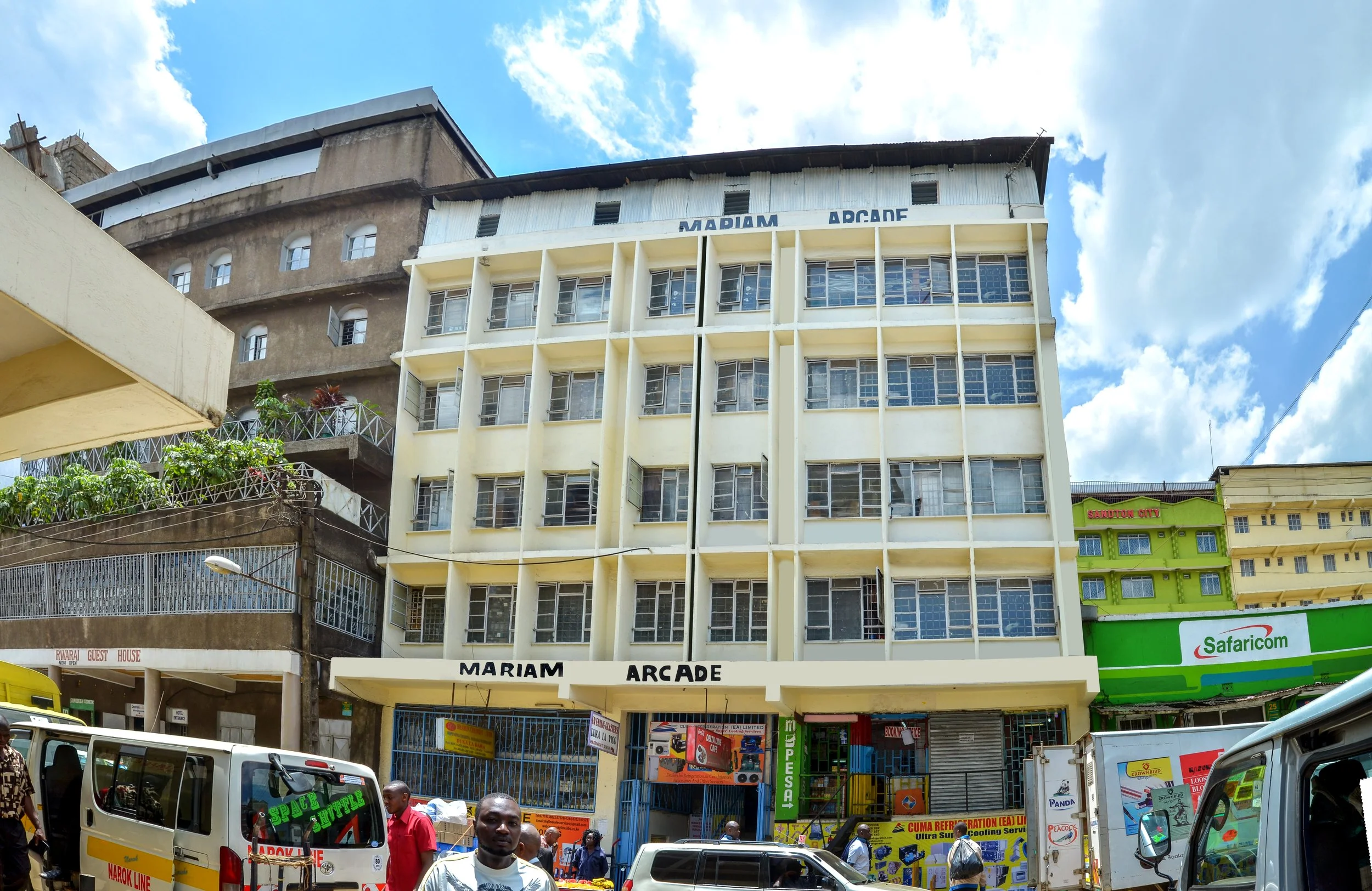 A multi-story commercial building with the sign 'Mariam Arcade' at the front, situated in a busy city street with cars and pedestrians.