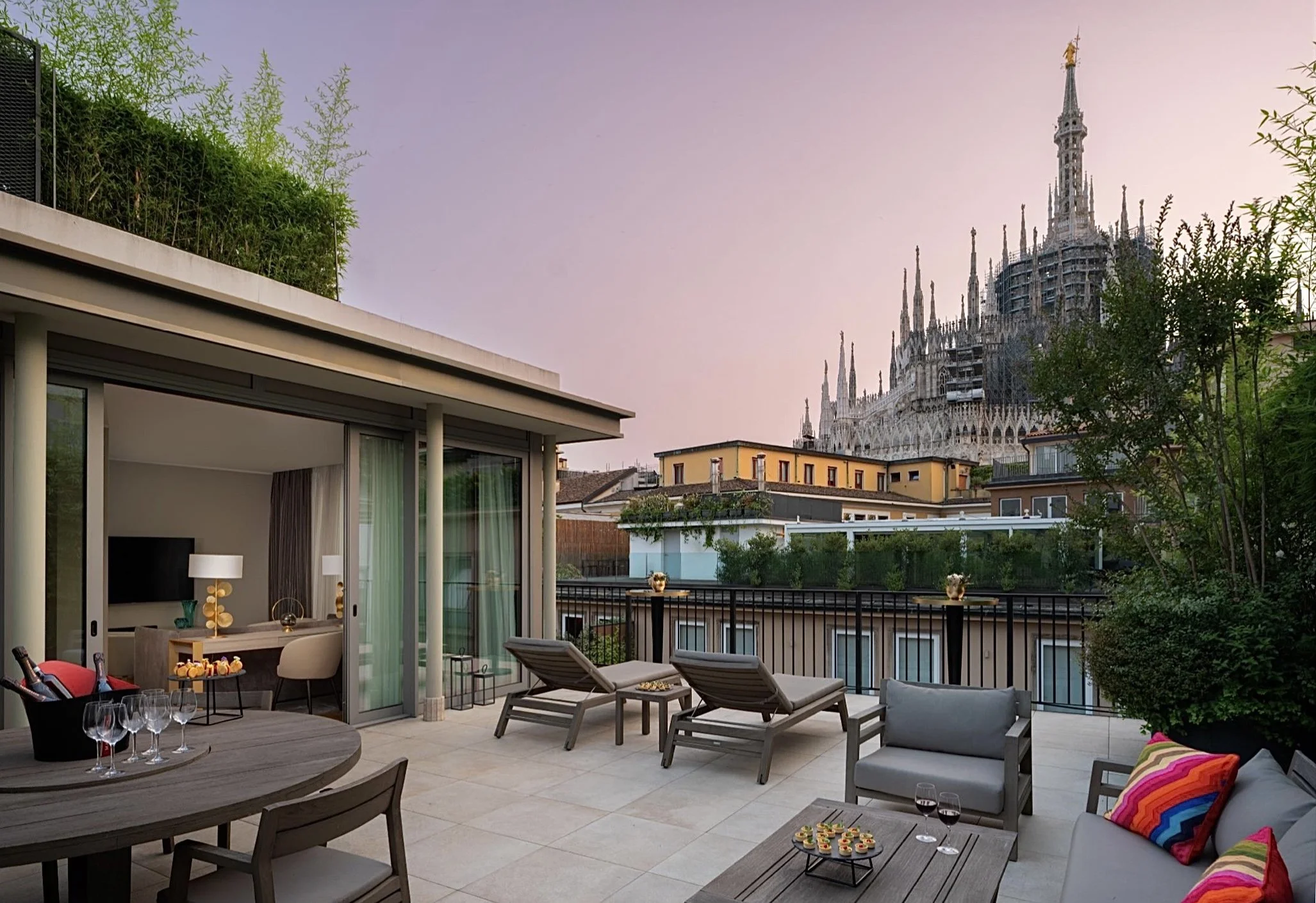Terrazza moderna con sedie, tavolo e cuscini colorati, con vista sul Duomo di Milano al tramonto.