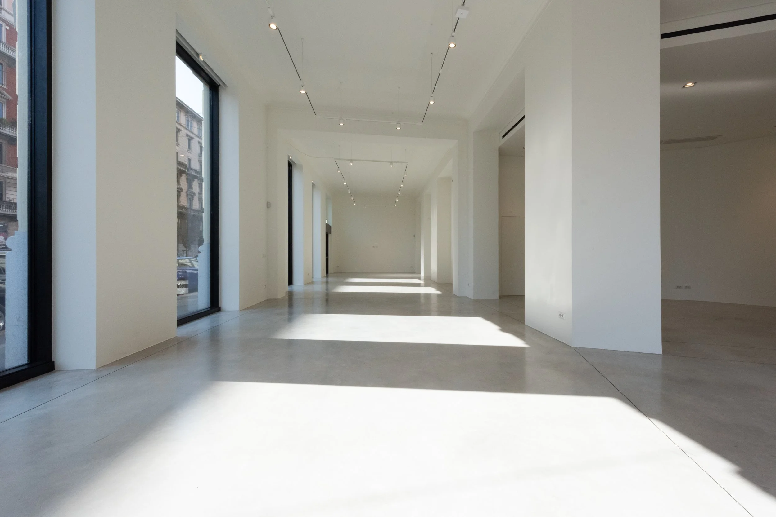 Interno di un edificio moderno con grandi finestre che lasciano entrare molta luce naturale, pareti bianche e pavimenti lisci. L'ambiente è spazioso e minimalista.