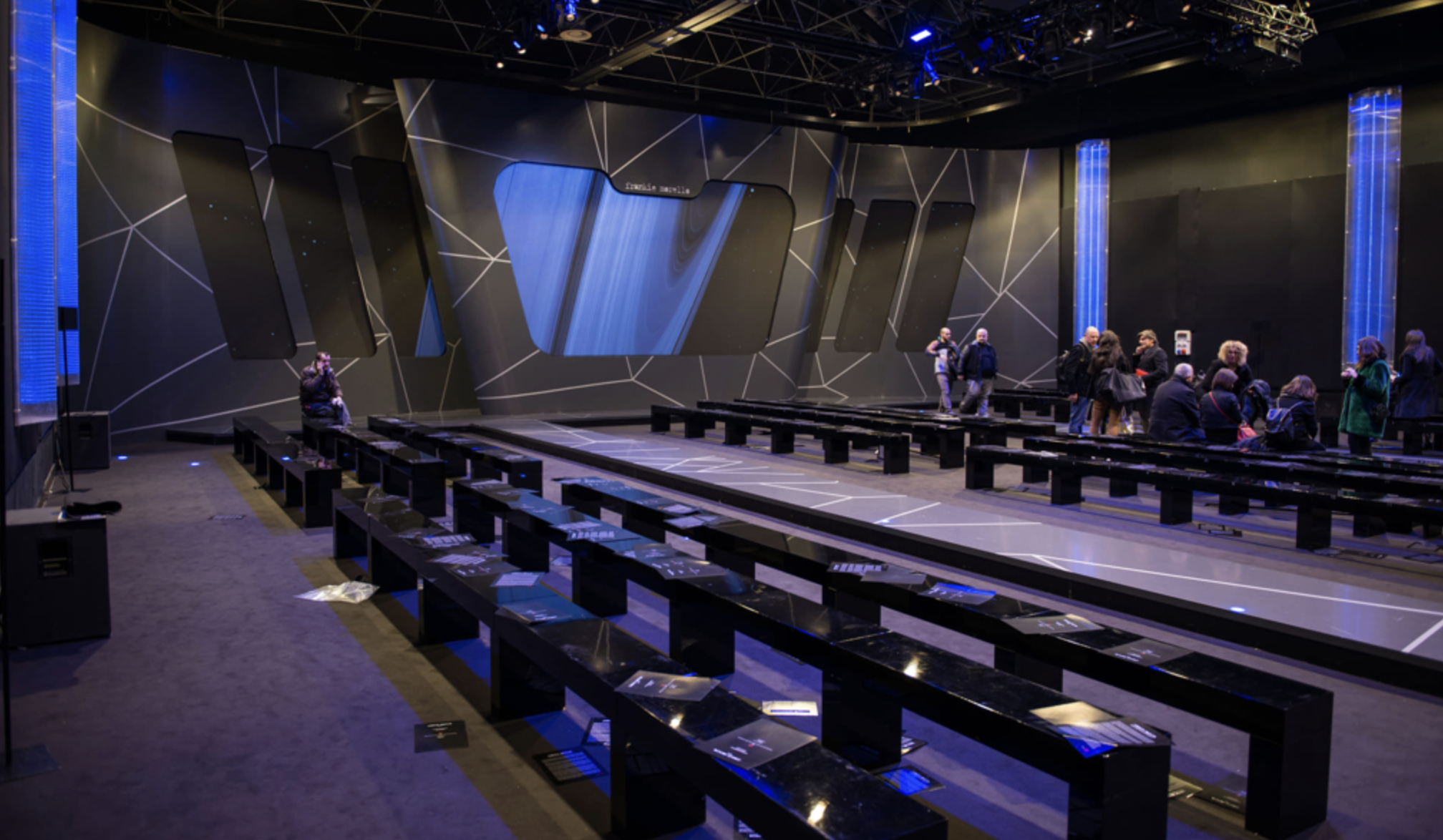 Sala di esposizione con pannelli digitali e persone che osservano gli schermi.