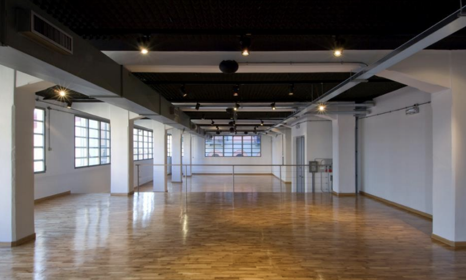 Spazio vuoto con parquet di legno, grandi finestre e illuminazione a soffitto, probabilmente un'aula o studio open space.