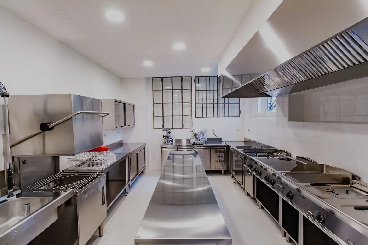 Cucina professionale con attrezzature in acciaio inox, piani di lavoro, forno, grill, e cappe di ventilazione.
