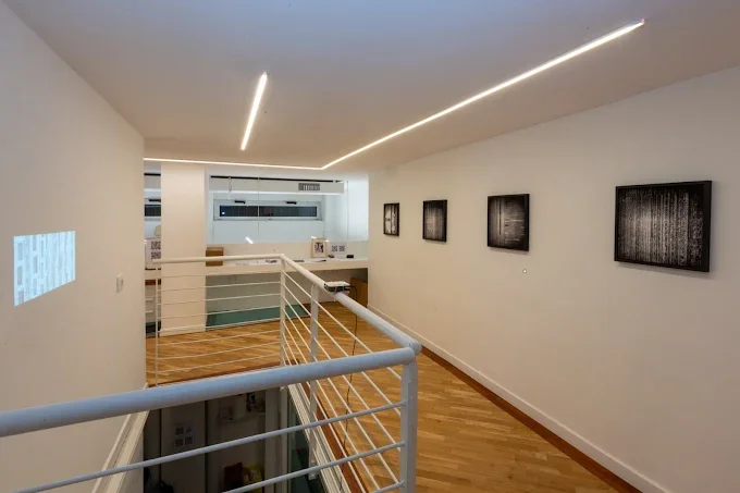 Galleria d'arte moderna con pareti bianche, dipinti o fotografie in cornice nera e pavimento in legno.