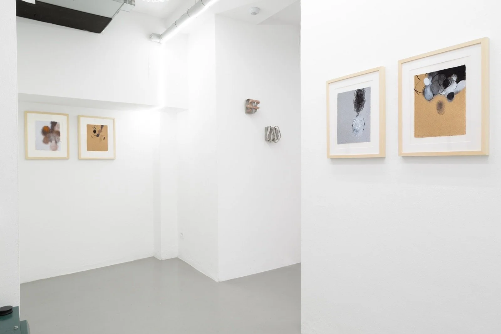 Galleria d'arte con quattro quadri astratti appesi alle pareti bianche, con un angolo della stanza visibile.