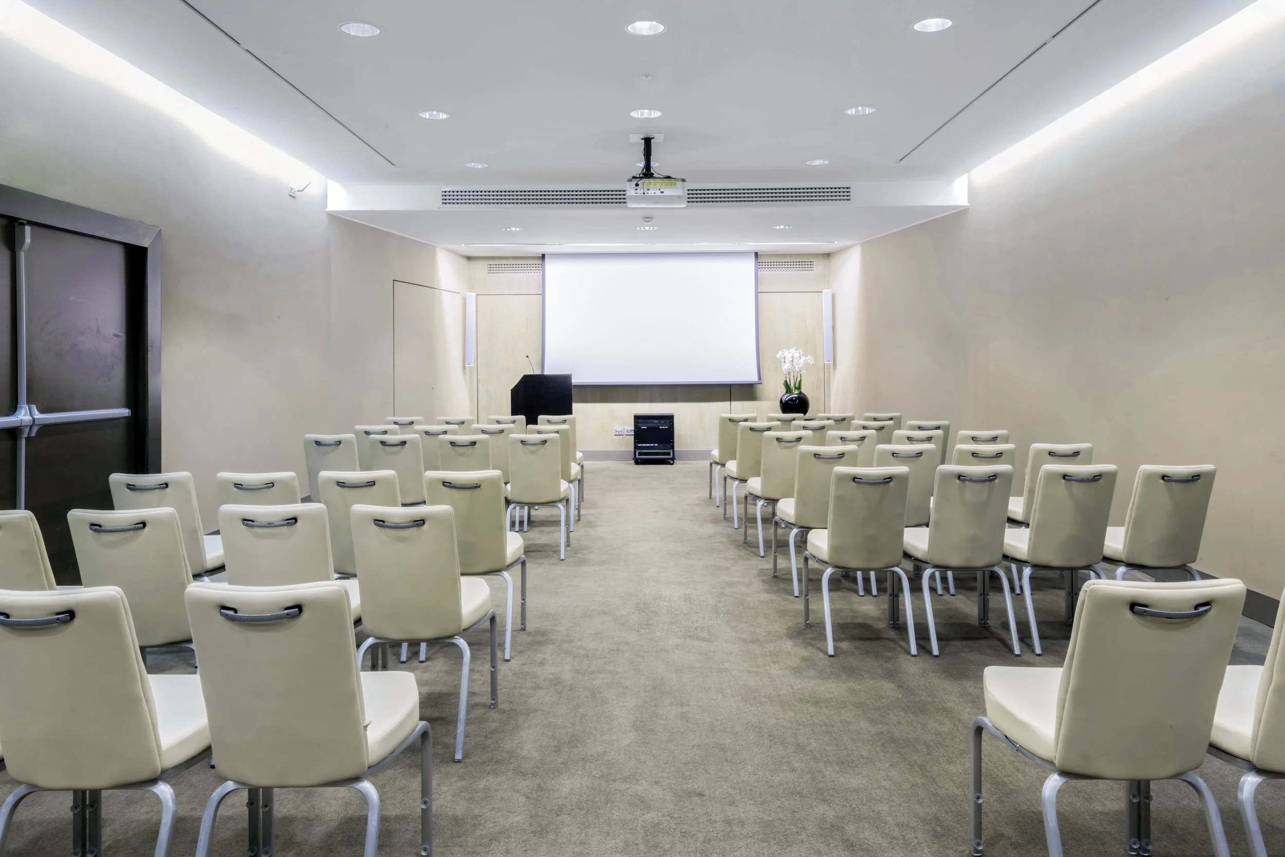 Sala conferenze con sedie beige disposte in ordine e grande schermo bianco sullo sfondo