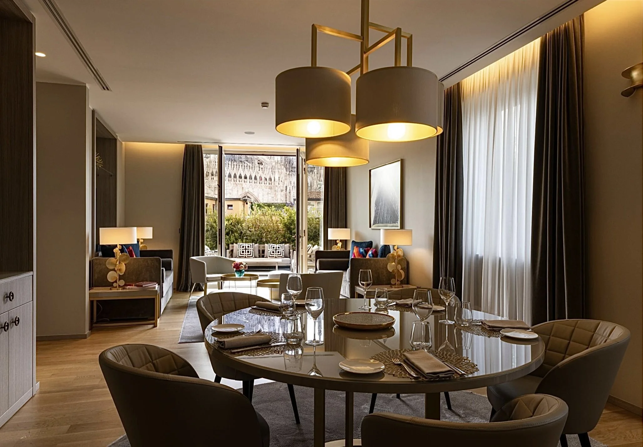 Interior di un soggiorno e sala da pranzo elegante e moderna con tavolo apparecchiato, luci a soffitto e grandi finestre con tende.