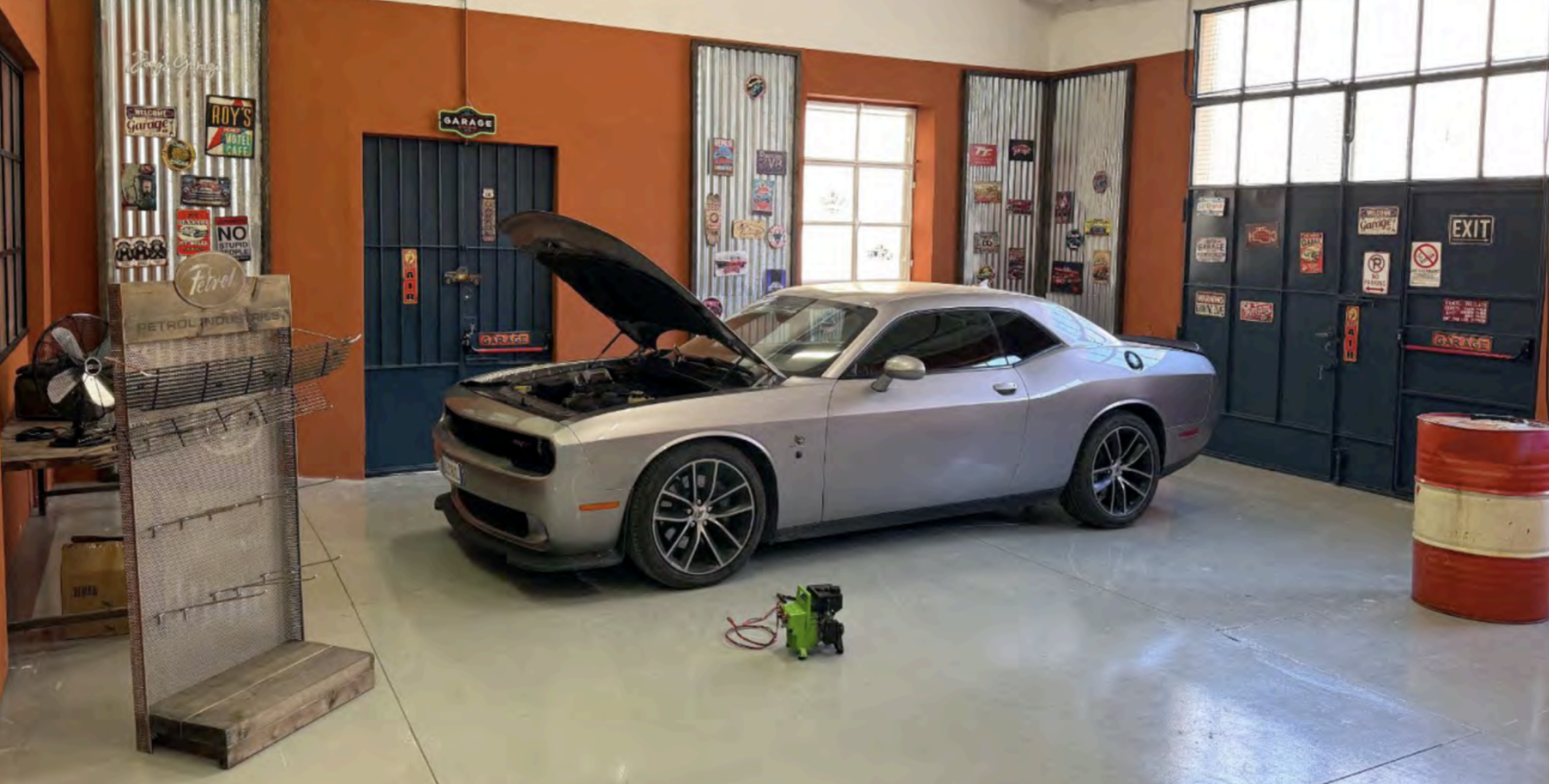 Auto da corsa di colore grigio all'interno di un garage con pareti arancioni e decorazioni vintage. Il cofano dell'auto è aperto e si vede il motore.
