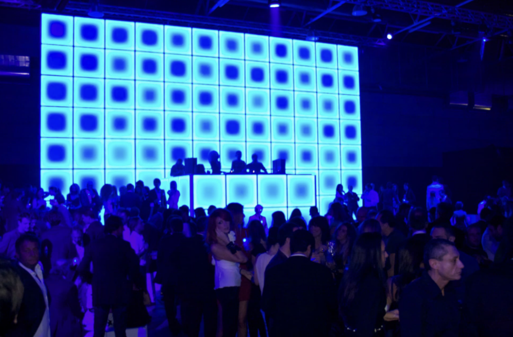 Festa con DJ in un locale con parete di luci blu e molte persone che socializzano