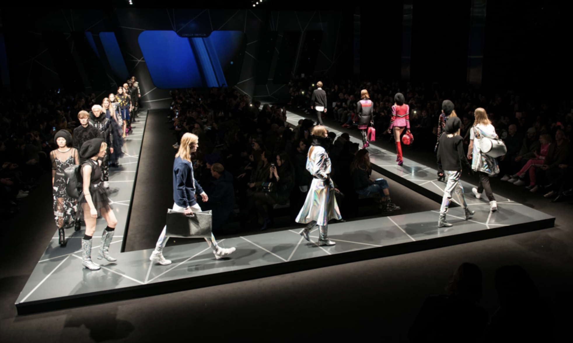 Passeggiata sulla passerella di moda con modelli che indossano abiti diversi davanti a un pubblico in un evento di sfilata.