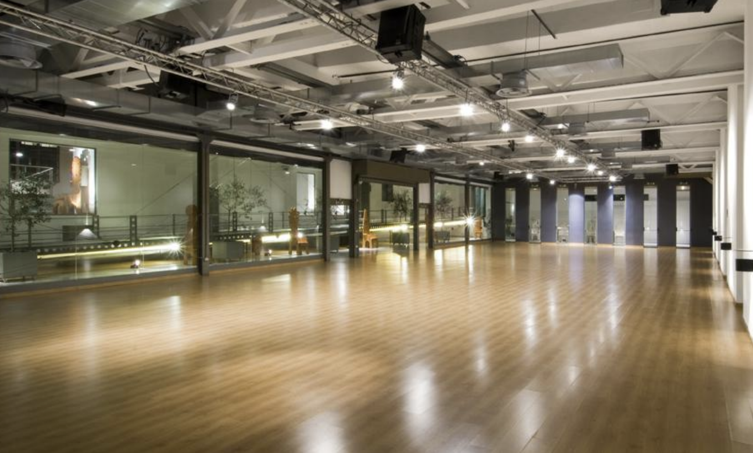 Sala vuota con pareti di vetro, pavimento di legno e luci sospese.