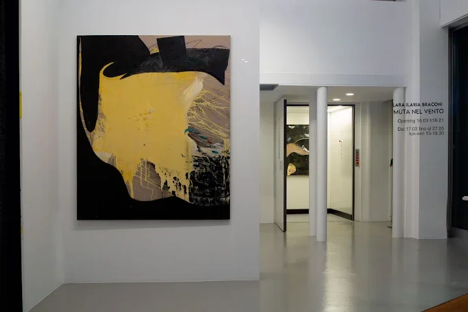 Un quadro astratto con colori nero, giallo e beige appeso a una parete bianca di un'arte contemporanea in una galleria.