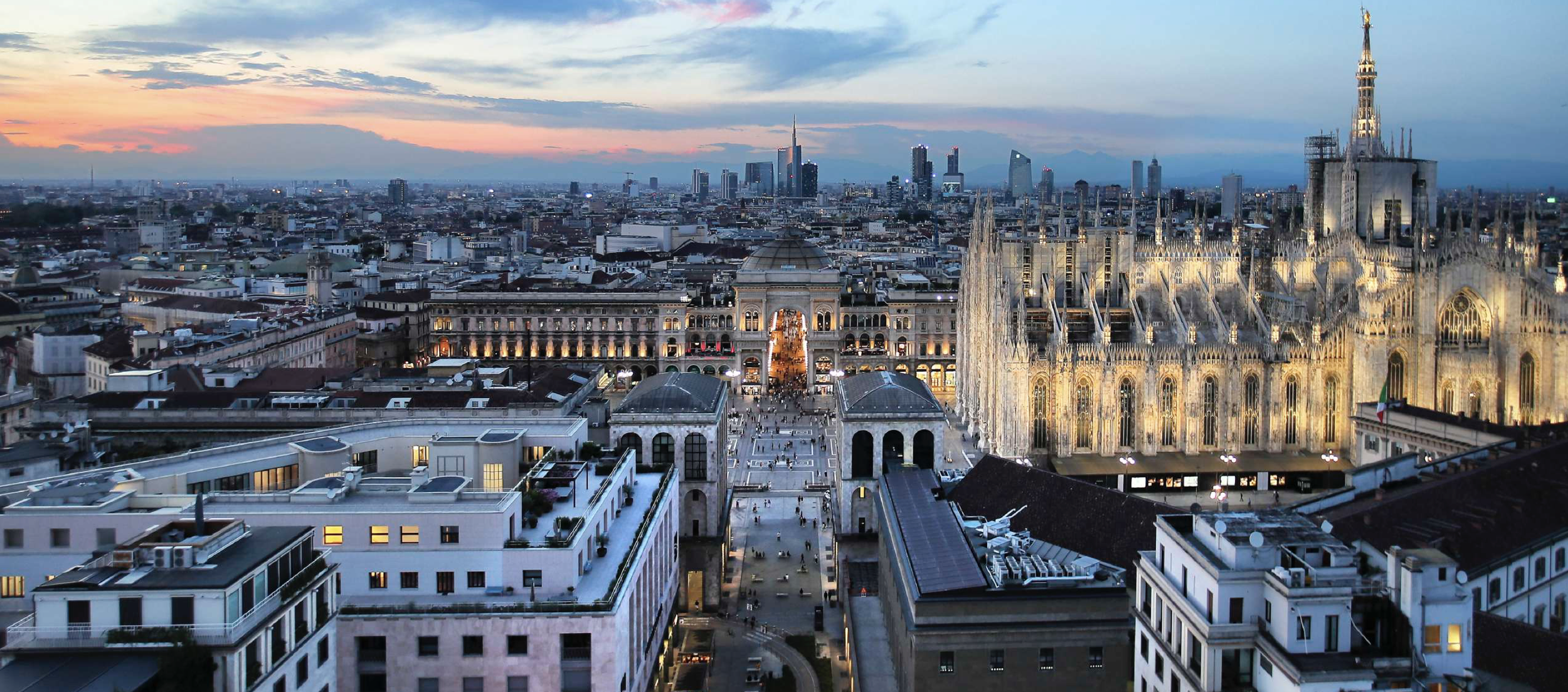 Panoramica del Duomo di Milano al tramonto, con la città moderna sullo sfondo.