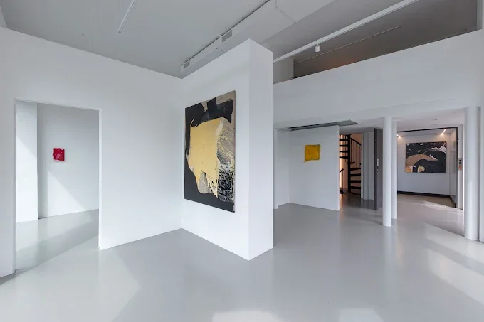 Interno di una galleria d'arte con pareti bianche e opere d'arte astratte esposte.