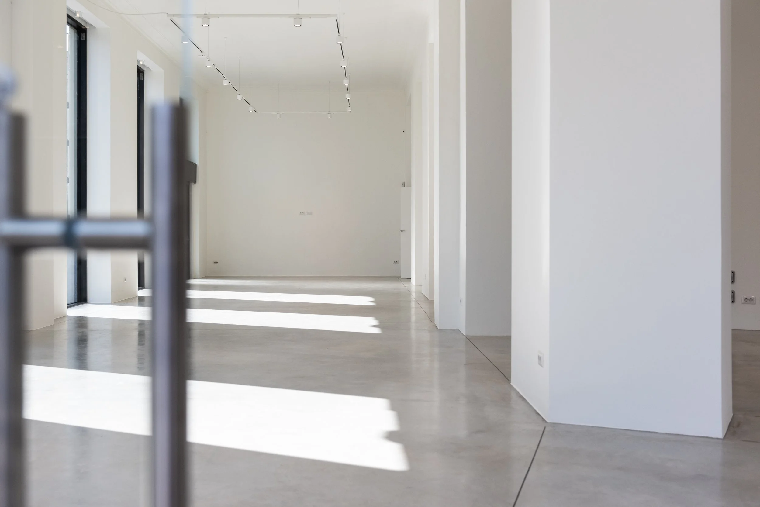 Interno di uno spazio vuoto e moderno con pareti bianche, grandi finestre e luci a soffitto.