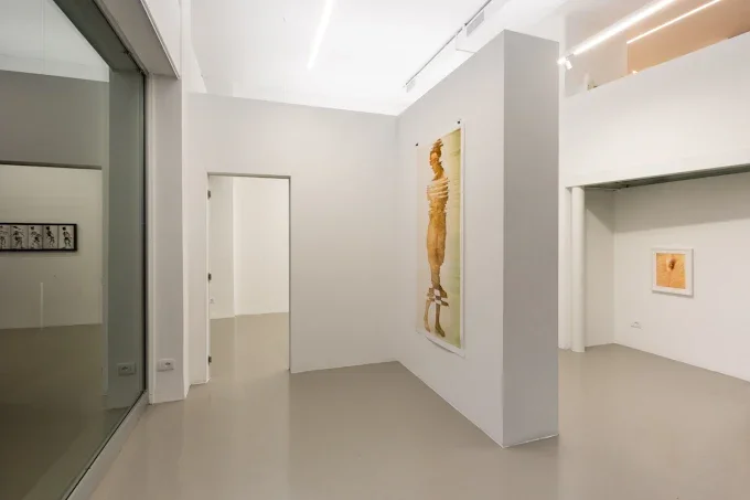 Interno di una galleria d'arte con pareti bianche e opere d'arte alle pareti, con un angolo visibile e una porta aperta