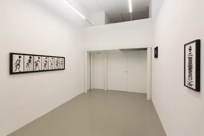 Una galleria d'arte moderna con opere minimaliste in bianco e nero su pareti bianche.