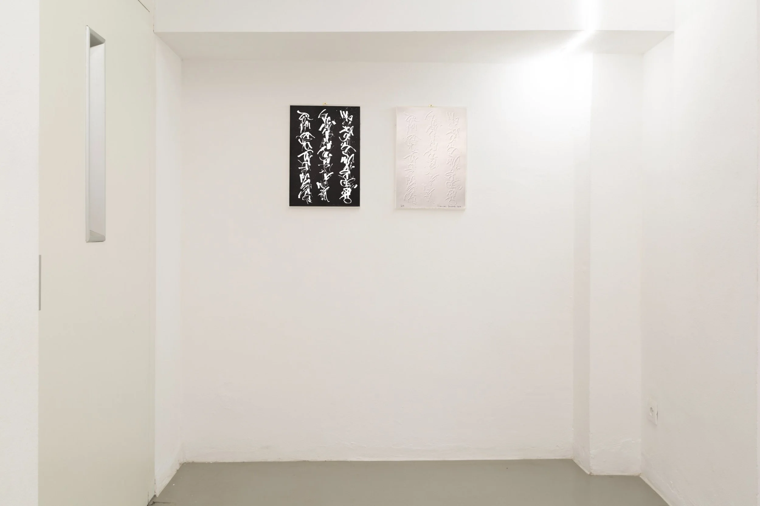 Due tele dipinte con calligrafia astratta, una nera e una bianca, appendute a una parete bianca in una galleria d'arte.