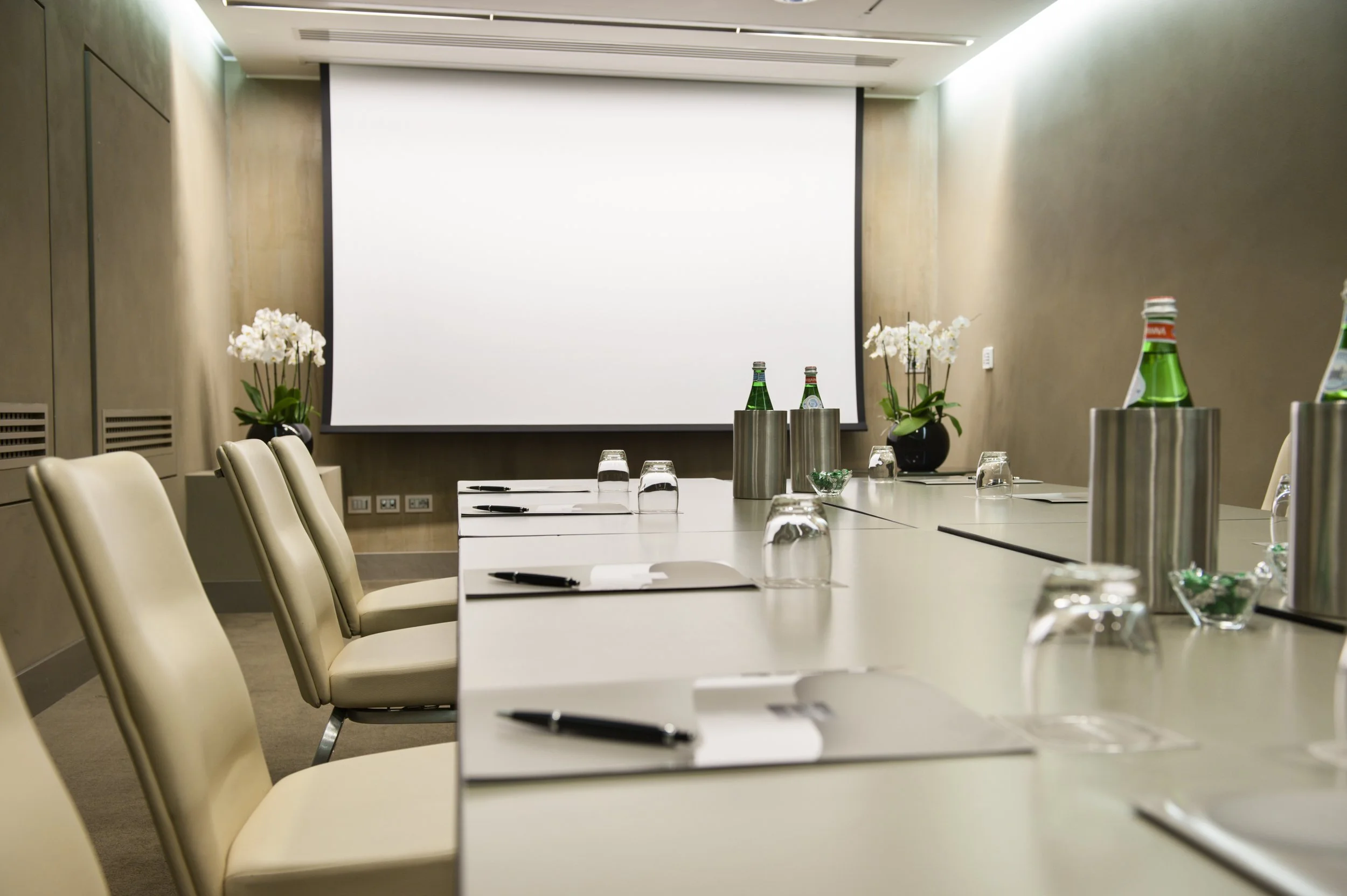 Sala riunioni con tavolo, sedie beige, premio acqua e bicchieri, decorata con piante di orchidea