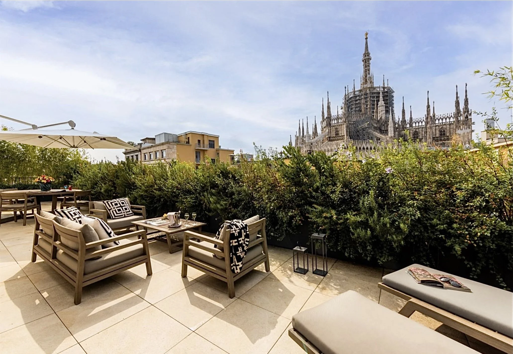 Terrazza arredata con poltrone, divani e tavolino, con vista sul Duomo di Milano e cielo sereno.