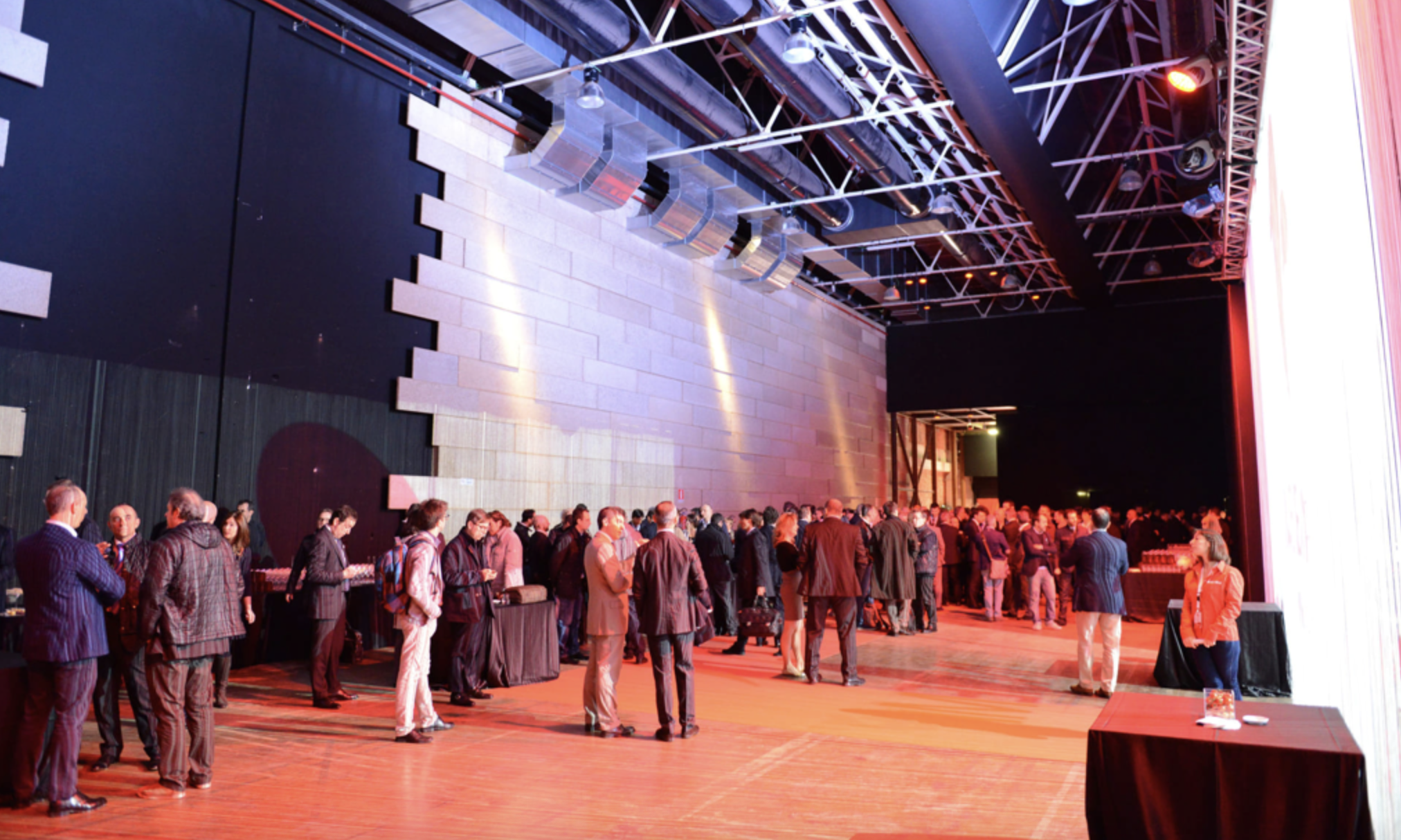 Un grande evento o conferenza con molte persone in attesa, in un ambiente moderno con pareti di mattoni e luci soffuse.