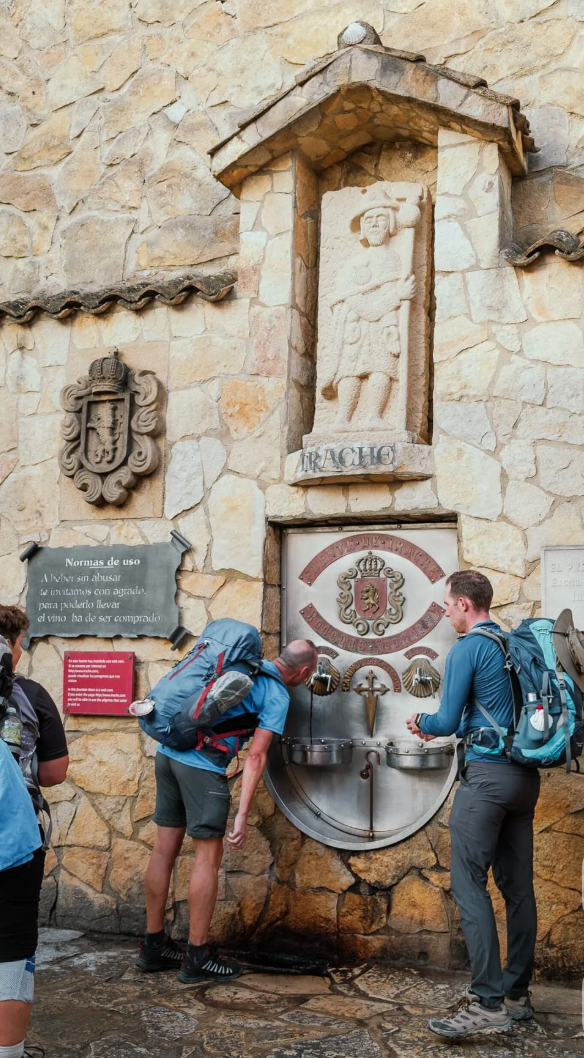 Groupe de marcheurs à Fuente Dé, Cantabrie, Espagne, près d'une fontaine publique en pierre avec des plaques et sculptures historiques.