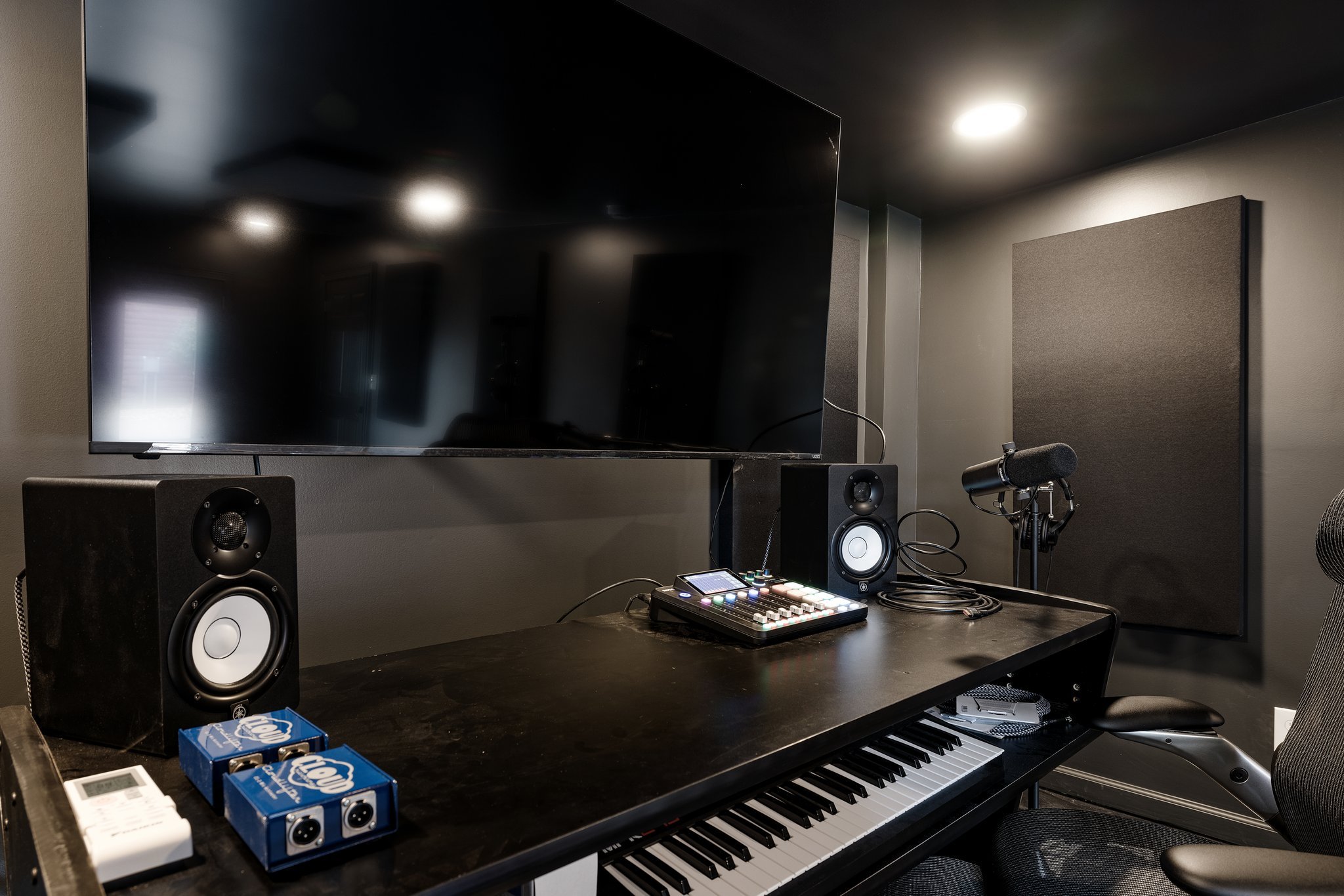 Music production studio with a keyboard, two speakers, a large monitor, a microphone, and audio equipment in a dark room.