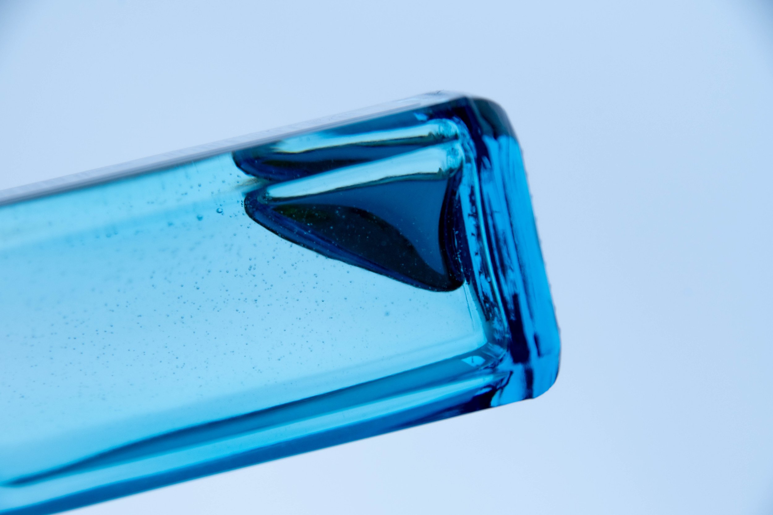 Nahaufnahme eines blauen, quadratischen Glasbehälters mit blauem Inhalt, Blick auf die obere Ecke gegen den Himmel