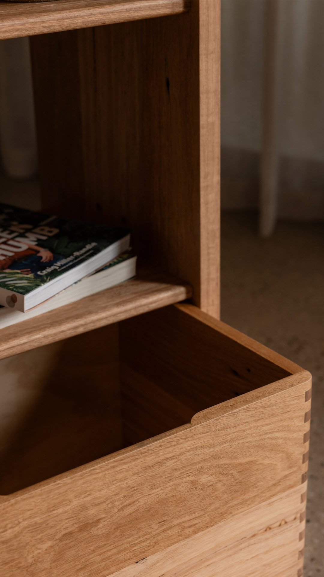 Close-up image of a reclaimed hardwood bookshelf with an open drawer at the bottom and some books on the shelf.