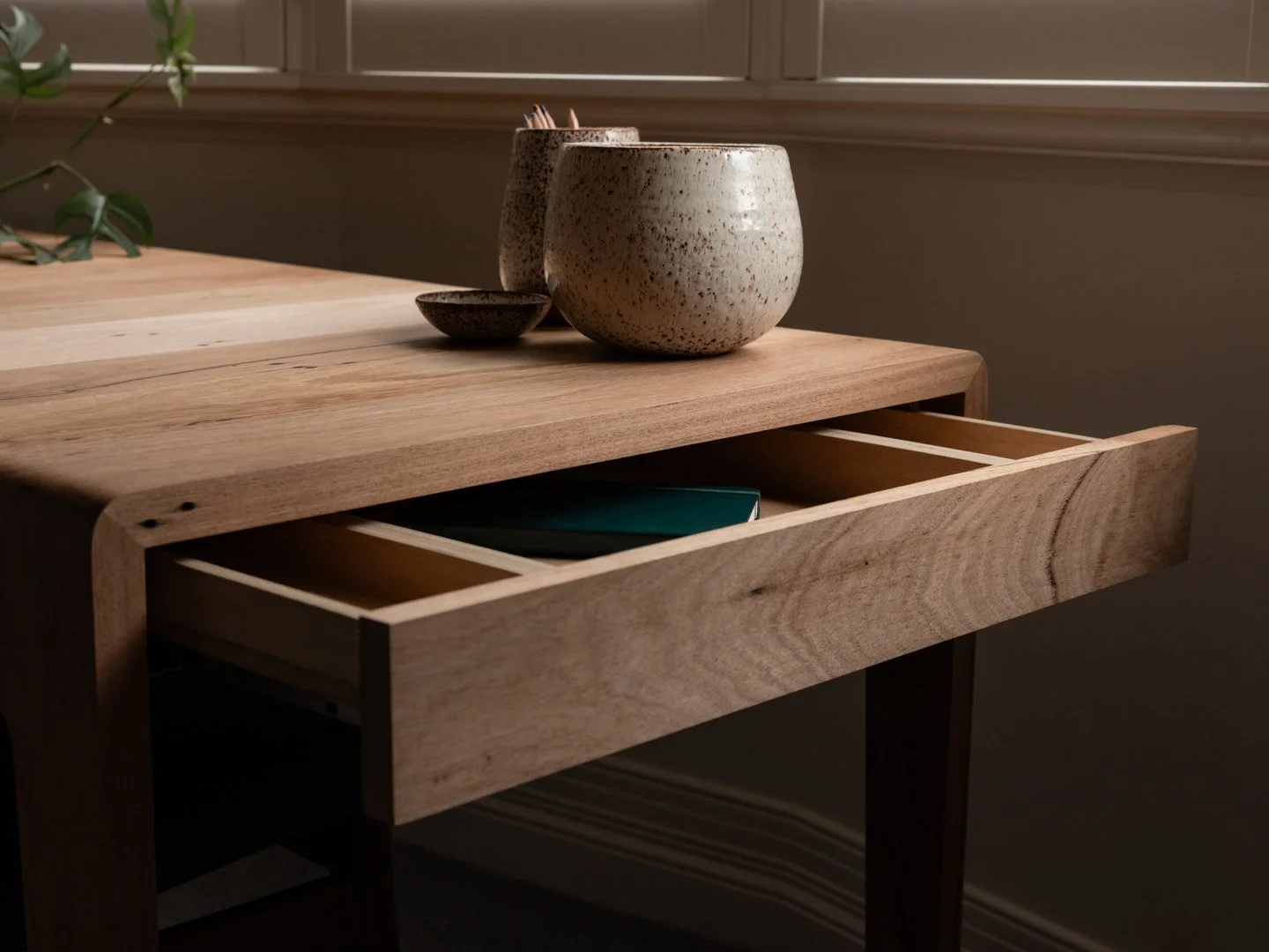 Wooden table with open drawer, displaying a closed notebook.