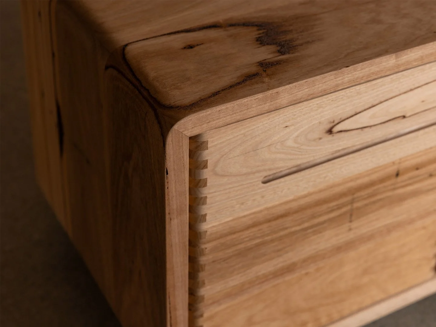 Close-up of a corner of a recycled hardwood cabinet, showcasing dovetail joints and natural wood grain.