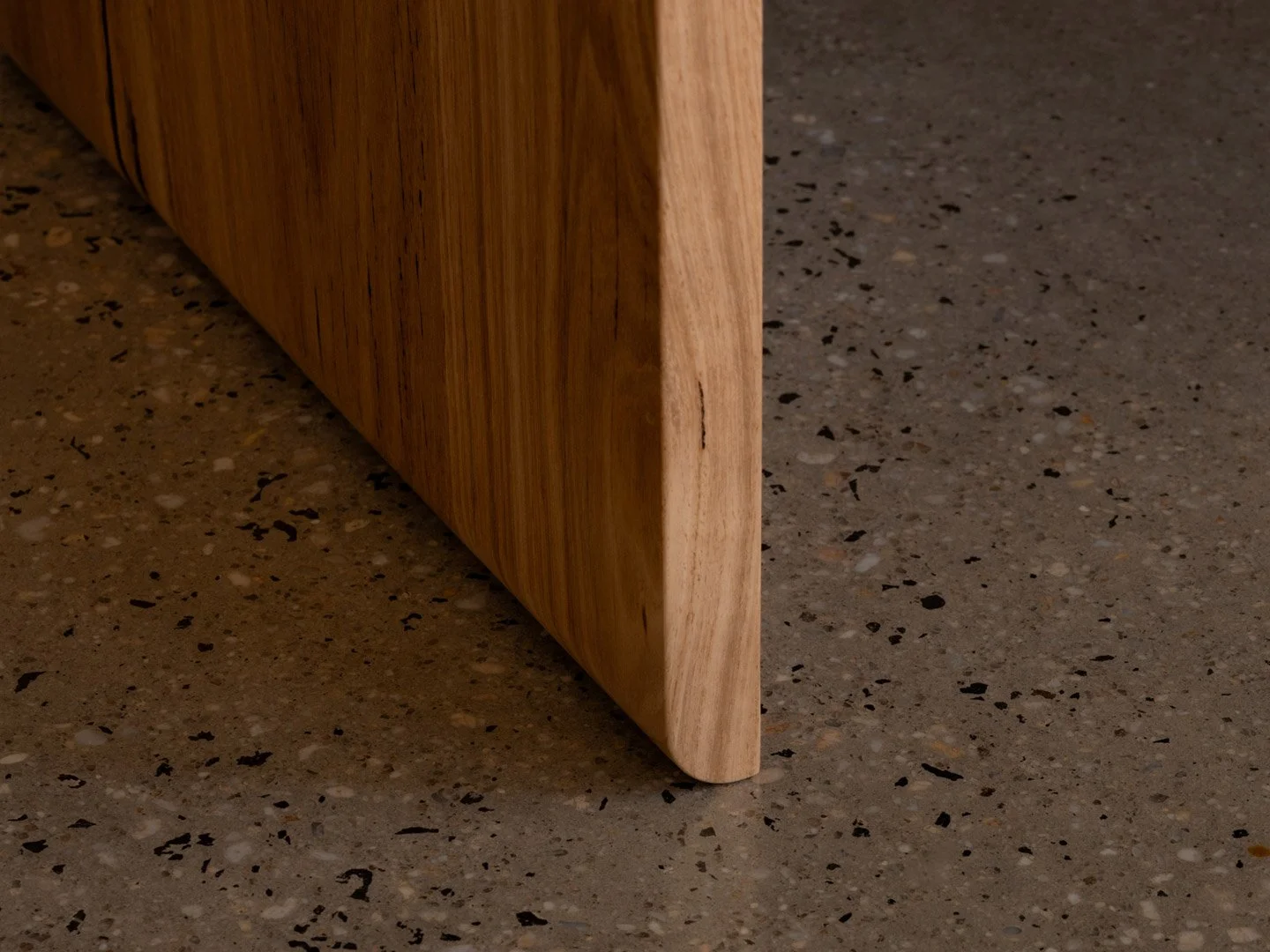 Close-up of a wooden furniture piece with a rounded corner on a speckled gray floor.