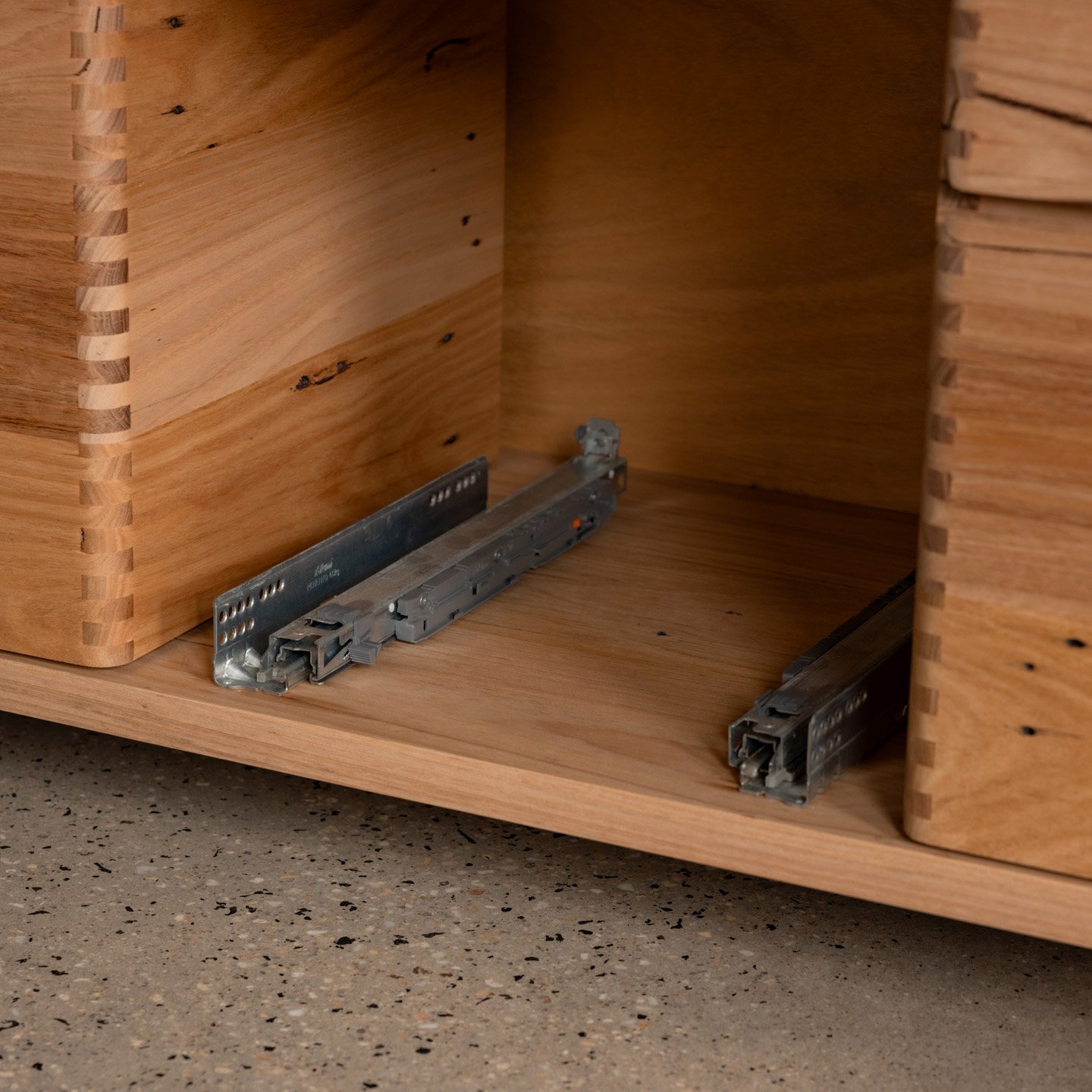 Inside of a wooden cabinet with metal drawer slides installed, but drawers are missing.
