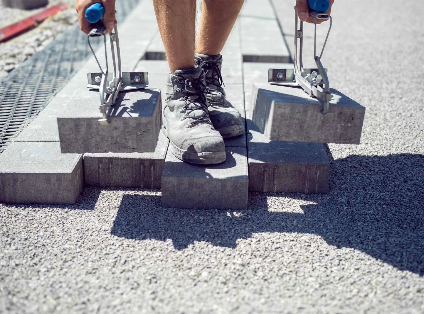 Person steht auf einem Bordstein und legt mit einer speziellen Vorrichtung die Oberseite einer Mauer aus Steinblöcken.