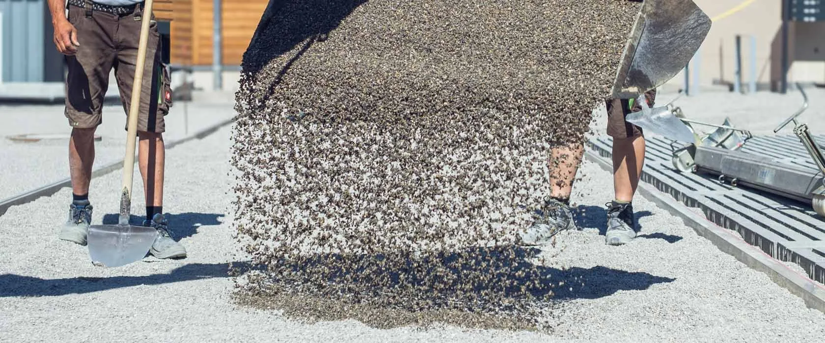Zwei Bauarbeiter verteilen Kies auf einer Baustelle im Freien