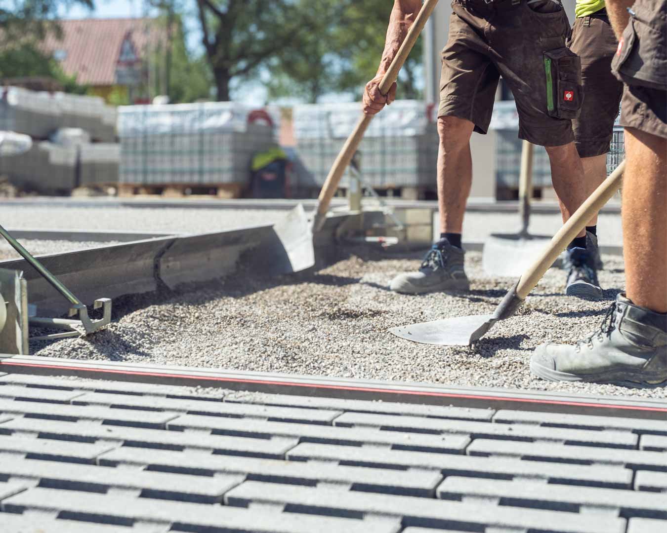 Menschen beim Verlegen von Pflastersteinen auf einer Straße bei gutem Wetter.