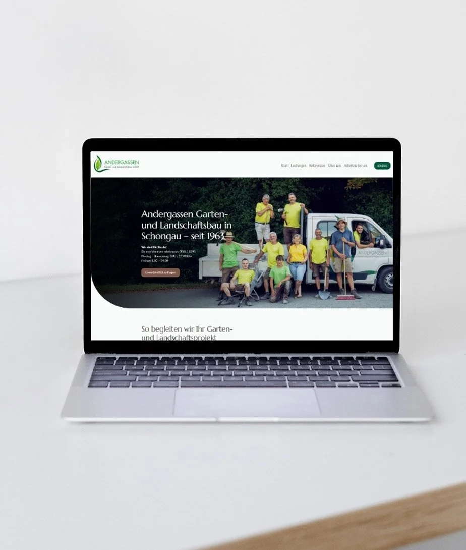 Laptop auf einem weißen Tisch zeigt eine Webseite der Firma Andergassen, die Garten- und Landschaftsbau in Schongau anbietet, mit einem Team von Mitarbeitern vor einem Firmenfahrzeug.