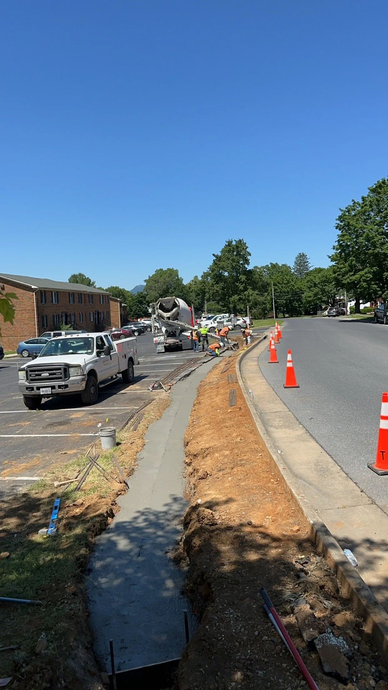 Construction workers building a sidewalk along a parking lot on a sunny day.