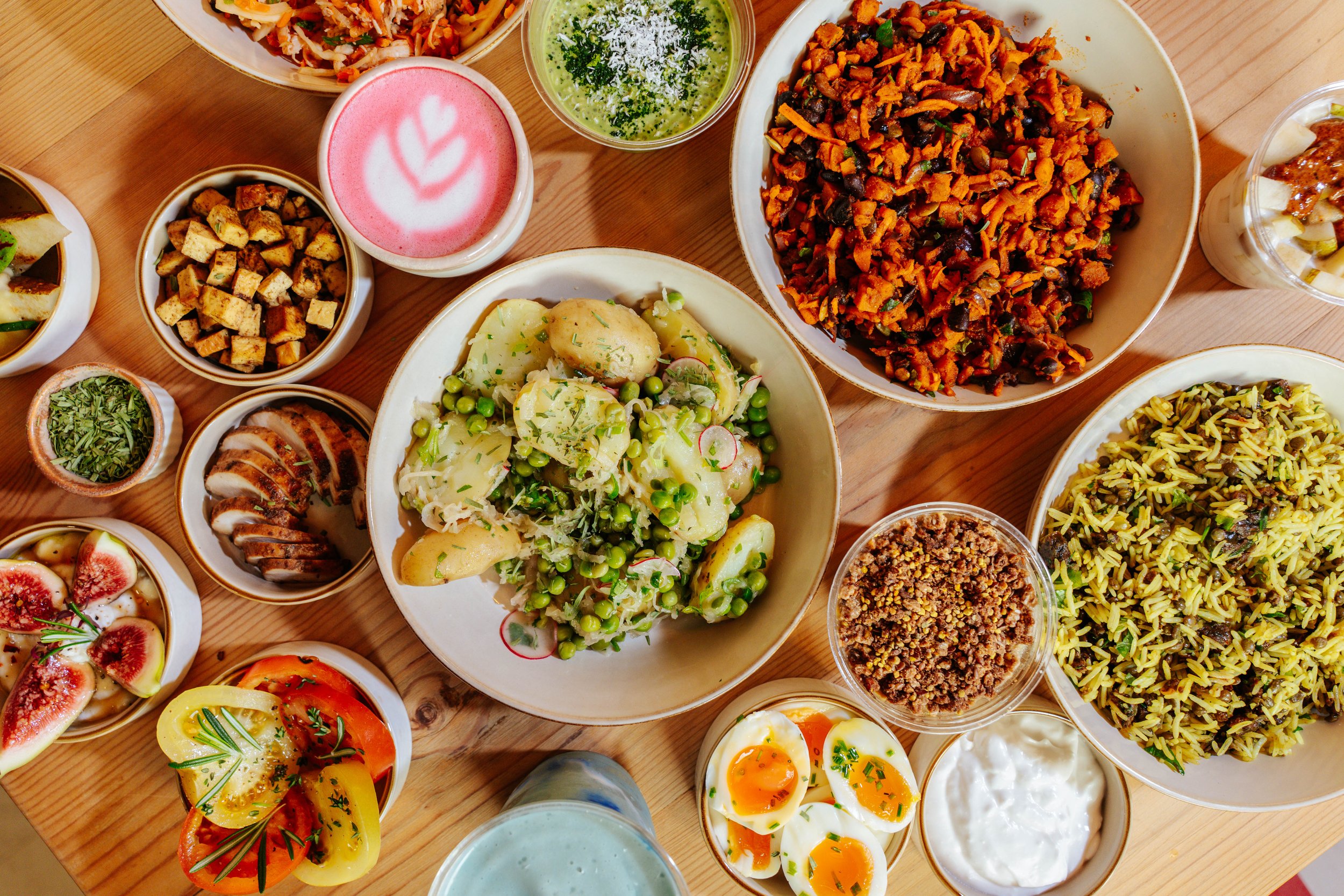 A variety of Middle Eastern dishes on a wooden table, including rice, salad, roasted vegetables, and several bowls of hot and cold appetizers.
