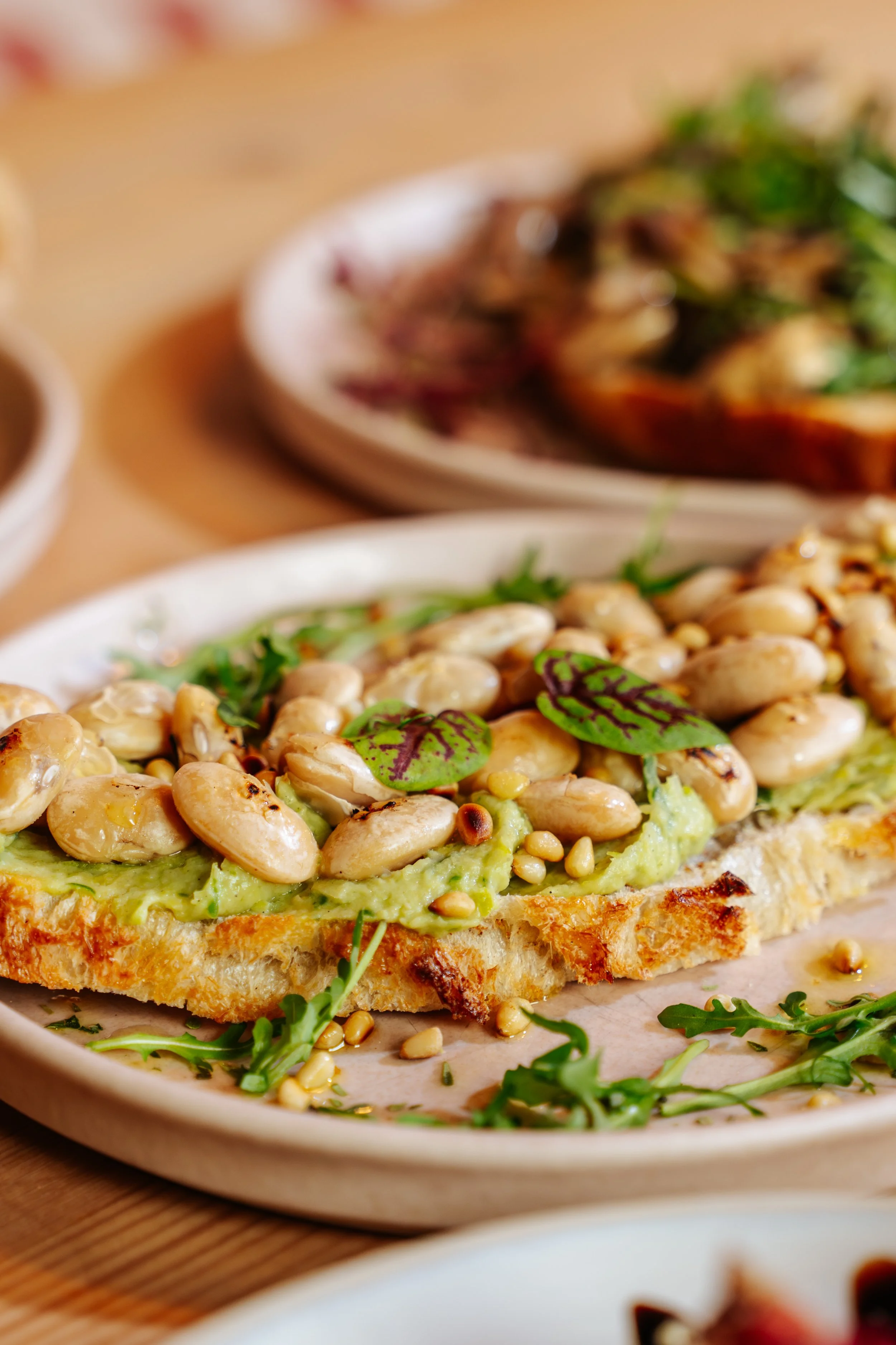 Open-faced avocado toast topped with pine nuts and microgreens, served on a white plate.