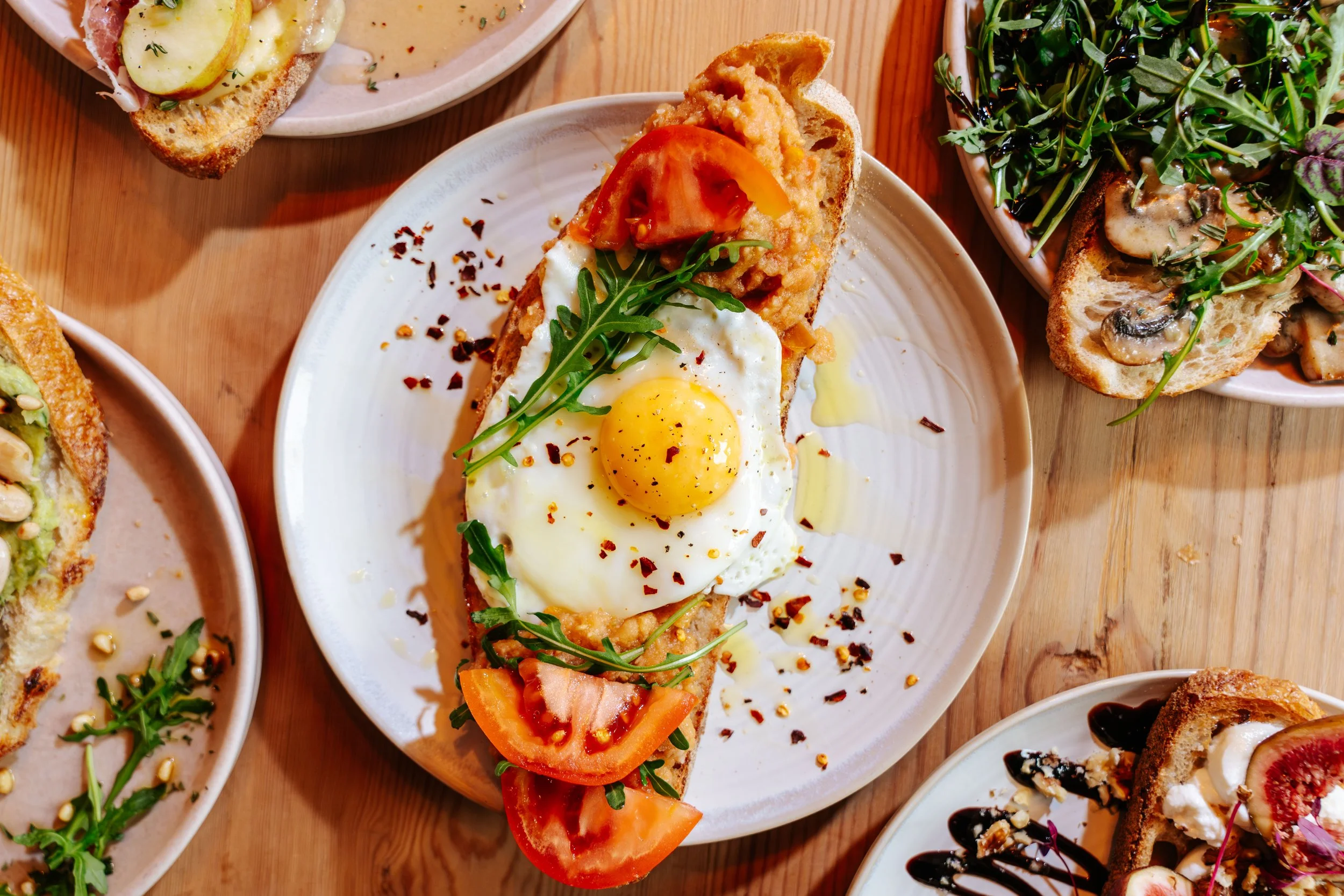 Open-faced breakfast sandwich with fried egg, tomato slices, arugula, on toasted bread, served on a white plate.